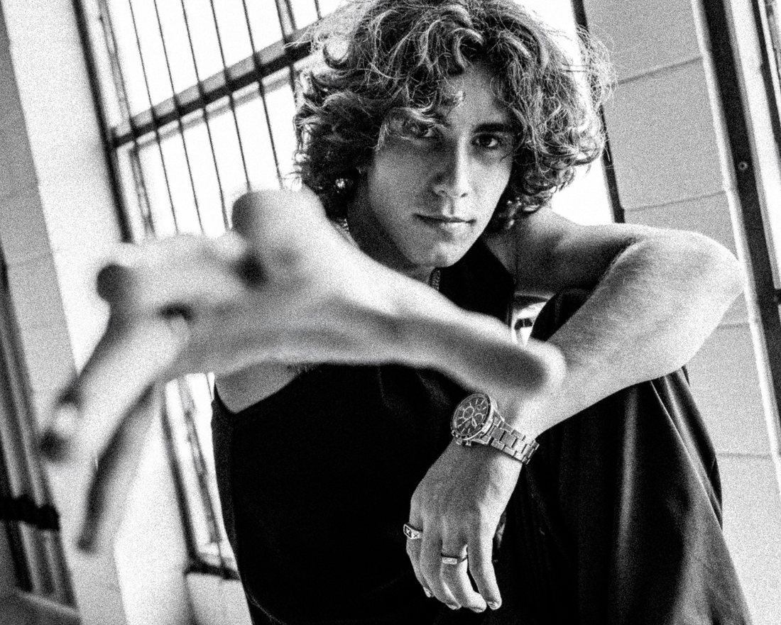 MYLES · B&W portrait, hand toward camera, barred window